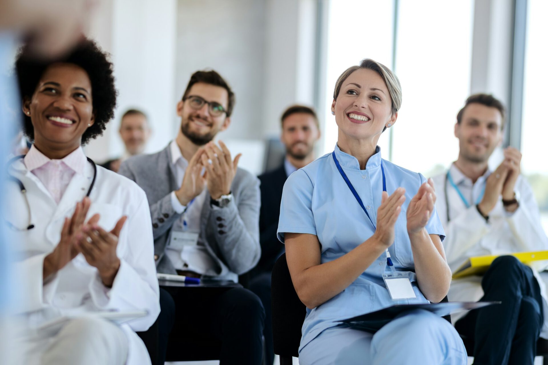 Group of happy healthcare workers applauding while attending an educational event.